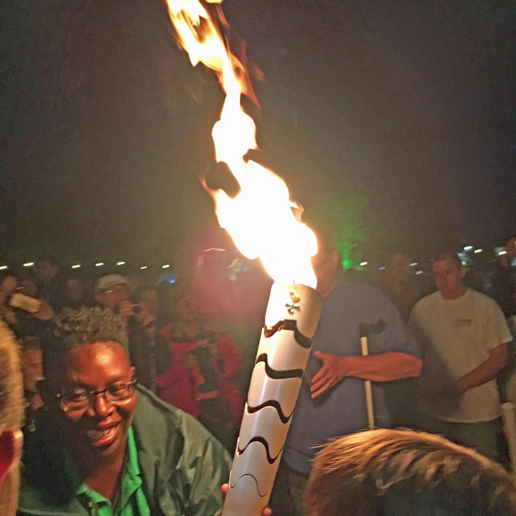 Woman with a flaming Paralympic torch. People in the background. 