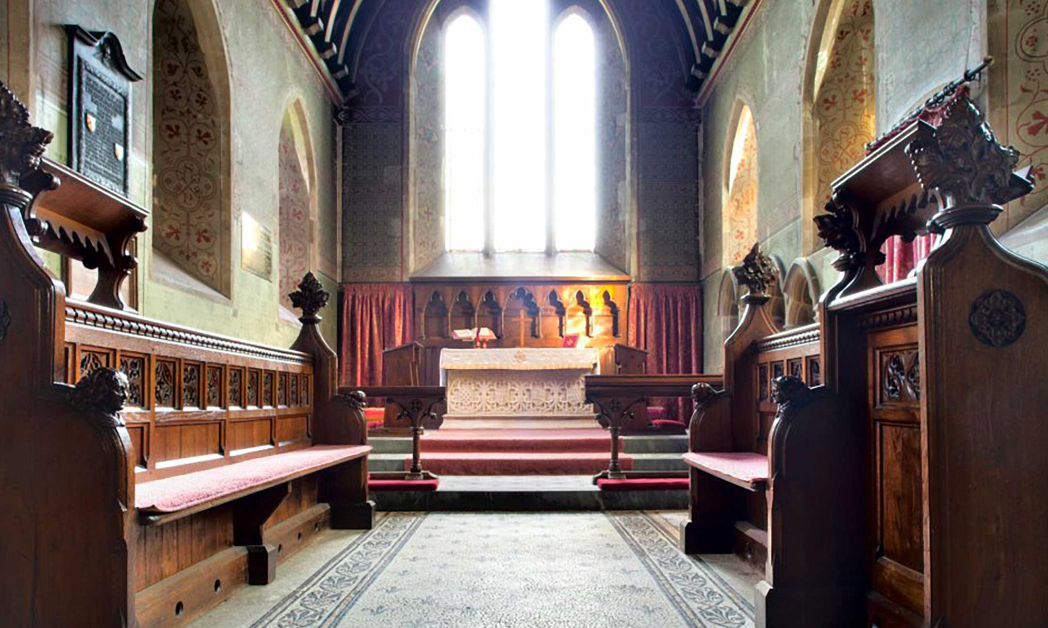 Colour photo of the inside of a church, looking towards a simple altar and stained glass window.