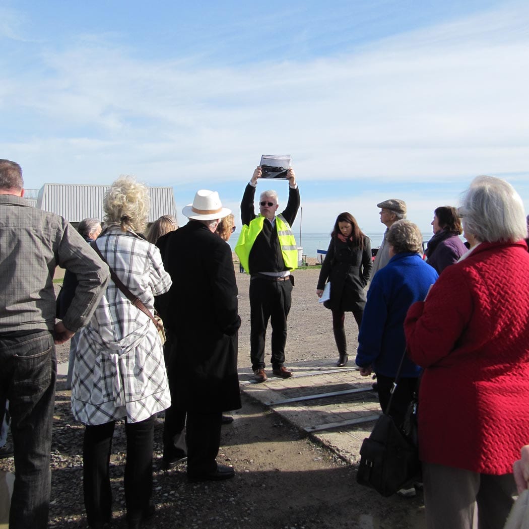 People standing on a beach looking at a man holding a sign up. A Bright Culture consultation event.