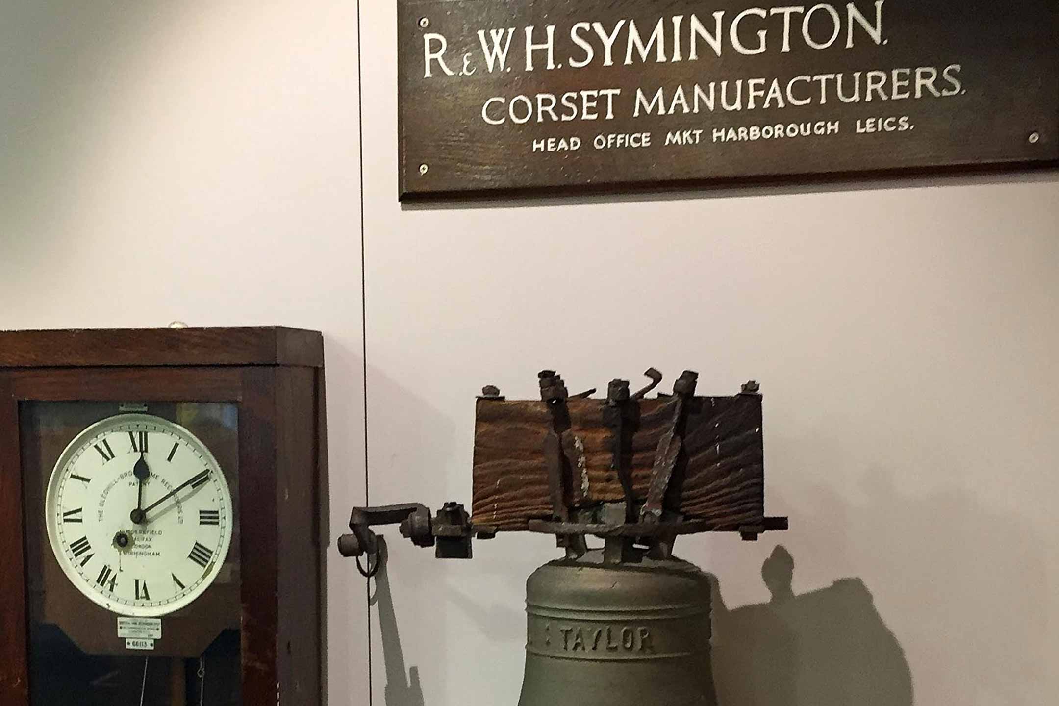 Wooden clocking in/out machine and a large bell. 