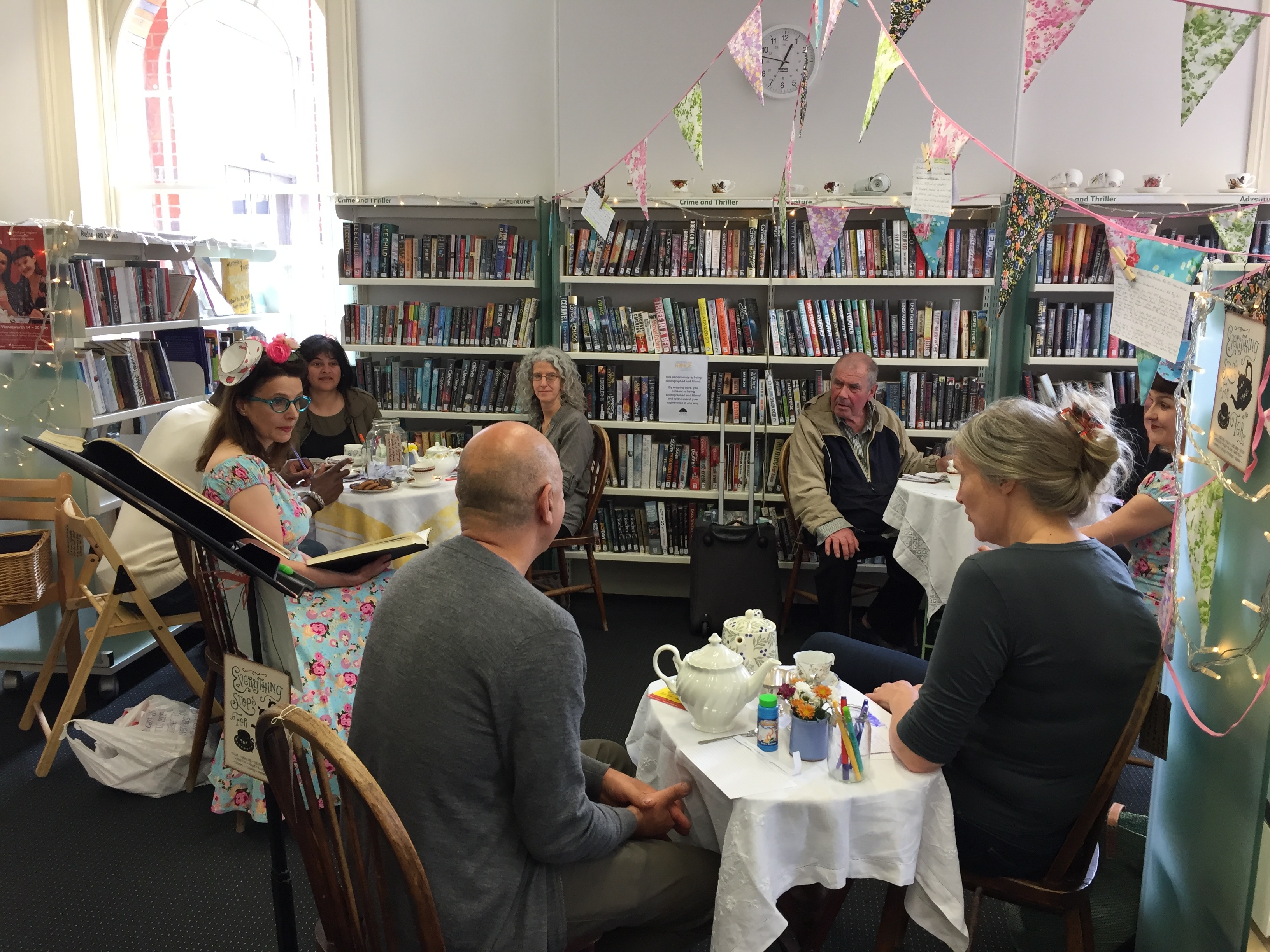 People sitting at tables drinking tea in a library.