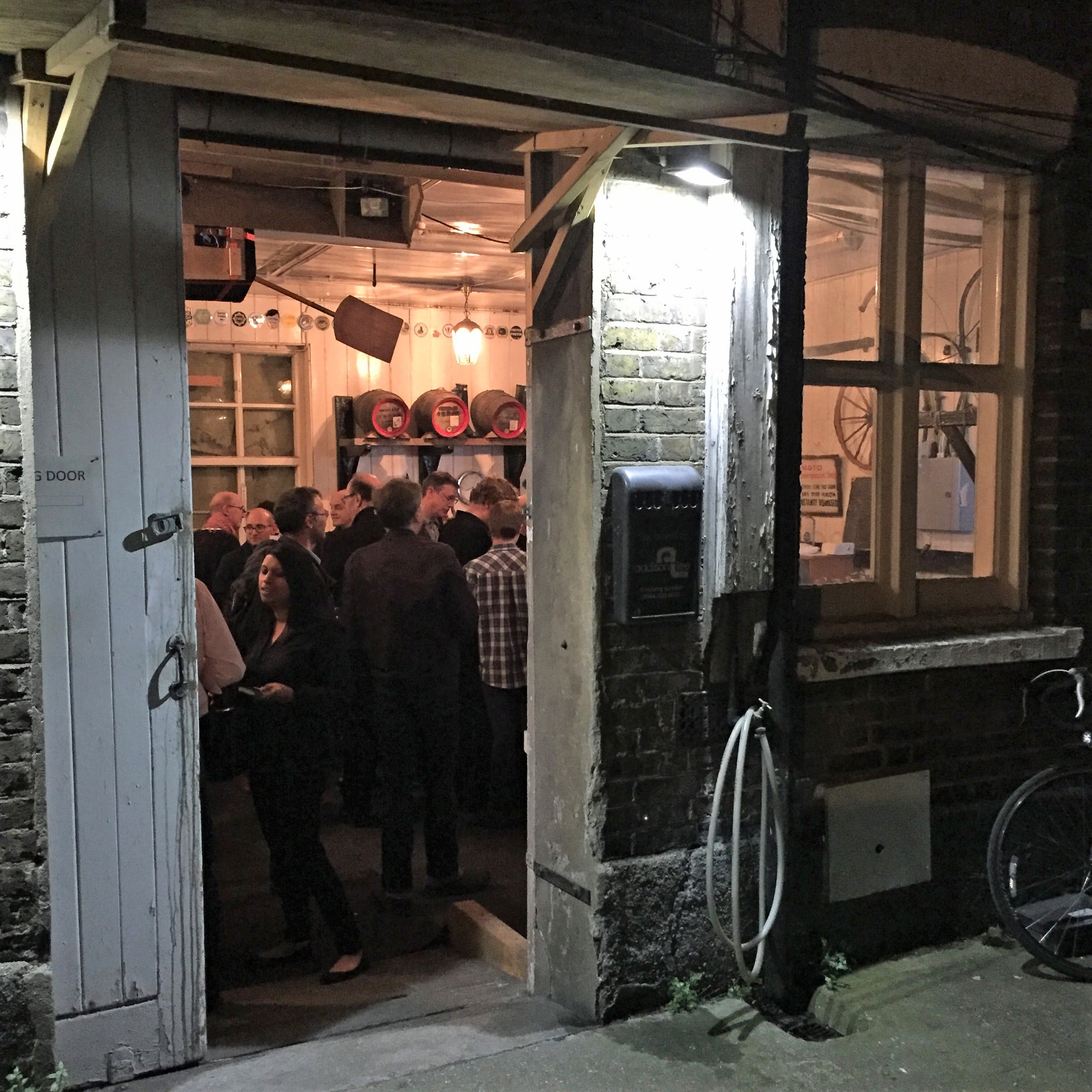 small brick building at night, with stable doors open and people standing inside.