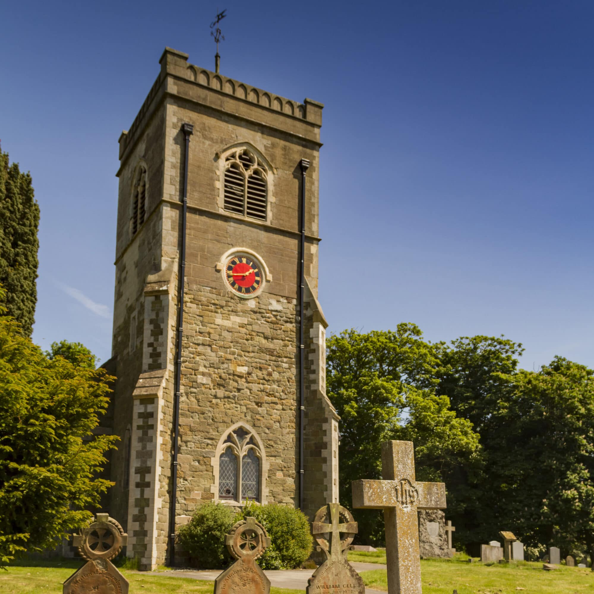 A square church tower, with a stone cross in the foreground. 