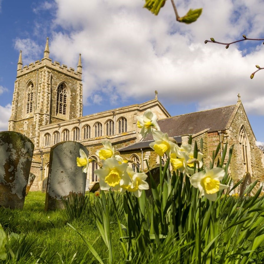 Large stone church with gravestones and grass in the foreground. 