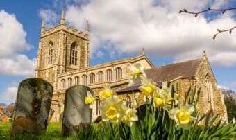 A large stone church with tower, with daffodils in the foreground.